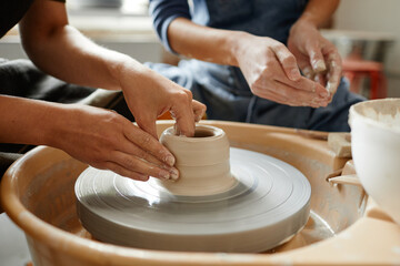 Close up young people working on pottery wheel together in handmade ceramics workshop, copy space