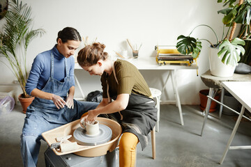Portrait of two young women working on pottery wheel together in handmade ceramics workshop, copy space - Powered by Adobe