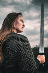 Portrait of woman in image of medieval warrior under dramatic sky. Beautiful woman in medieval...