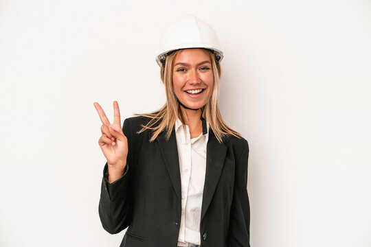 Young caucasian architect woman wearing a helmet isolated on white background joyful and carefree showing a peace symbol with fingers.