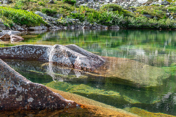 Fototapeta na wymiar Green lake with clear transparent water from which huge granite stones stick out