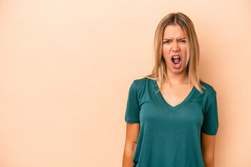 Young caucasian woman isolated on beige background shouting very angry, rage concept, frustrated.