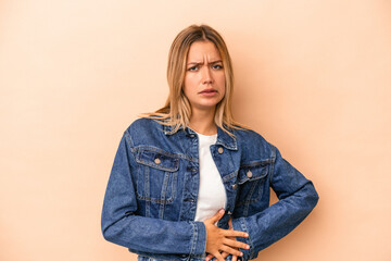 Young caucasian woman isolated on beige background having a liver pain, stomach ache.