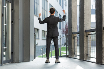 Fototapeta na wymiar Successful Caucasian businessman with arms up celebrating victory. Concept: success, career growth, victory, freedom. silhouette business man employee on background a modern office building. outside