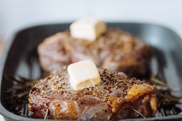cooking sumptuous steaks in a grill pan with butter spreading over the steak seasoned with ground pepper and salt with rosemary sprigs