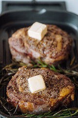 cooking sumptuous steaks in a grill pan with butter spreading over the steak seasoned with ground pepper and salt with rosemary sprigs