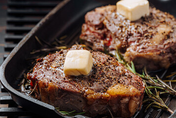 cooking sumptuous steaks in a grill pan with butter spreading over the steak seasoned with ground pepper and salt with rosemary sprigs