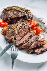juicy well-fried ribeye steaks on a white platter on a white marble surface with raspmarine and fried cherry tomatoes and peppers. steaks are sliced and ready to serve