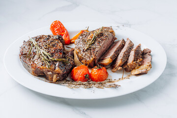juicy well-fried ribeye steaks on a white platter on a white marble surface with raspmarine and fried cherry tomatoes and peppers. steaks are sliced and ready to serve