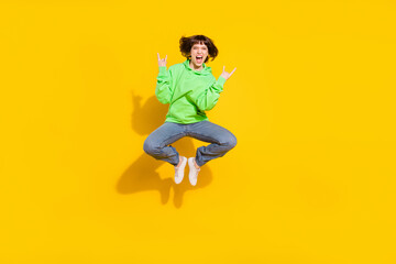 Full length body size view of pretty cheerful girl jumping showing horn sign having fun isolated over bright yellow color background