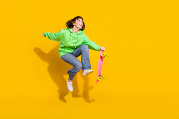 Fototapeta na wymiar Full length body size view of pretty cheery girl jumping riding skate having fun spare time isolated over bright yellow color background