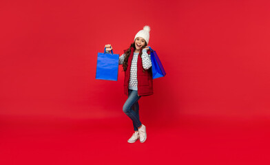 glad child in winter clothes hold shopping bags on red background with copy space, closeout