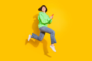 Fototapeta na wymiar Full length body size view of attractive cheery girl jumping using gadget 5g isolated over bright yellow color background