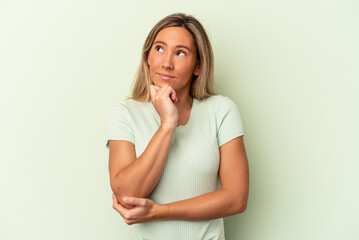 Young caucasian woman isolated on green background thinking and looking up, being reflective, contemplating, having a fantasy.