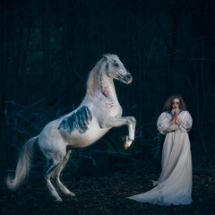 Obraz na płótnie Canvas Woman in a ghost dress and a dead white horse on its hind legs in the night forest
