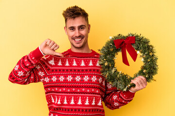 Young caucasian man holding a wreath isolated on yellow background feels proud and self confident, example to follow.
