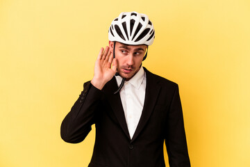 Young caucasian business man wearing a bike helmet isolated on yellow background trying to listening a gossip.