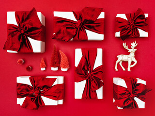 Top view of Christmas gift boxes laid out on a red background. Composition of gifts with red bows and ribbons, deer and artificial red fir-trees. 