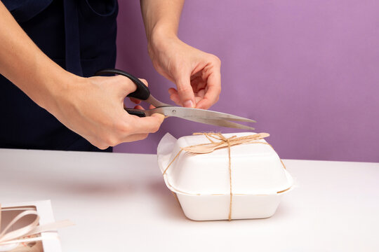 Hands Are Cut Off With Scissors String On Box With Bento Cake. Packaging For Delivery. Selective Focus.