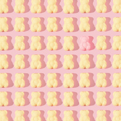 Creative pattern made with pastel yellow gummy bears and one pink gummy bear on pastel pink...