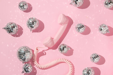 Christmas and New Year creative layout with disco ball decoration and pink retro phone hanset on pastel pink background. 80s or 90s aesthetic fashion concept. Minimal communication idea.