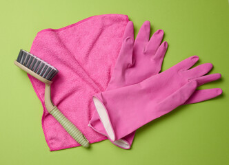 pink rug, rubber gloves for cleaning, brushes on a green background, flat lay.