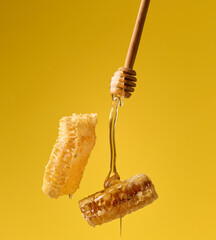 pouring transparent sweet honey from a wooden stick on a wax honeycomb. Yellow background. Food...