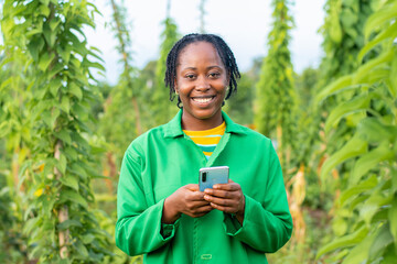 Shot of a happy female African farmer in Nigeria using her smartphone