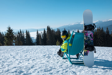 man snowboarder sitting in chair enjoying mountains view