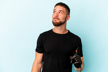 Young caucasian tattoo artist isolated on blue background dreaming of achieving goals and purposes