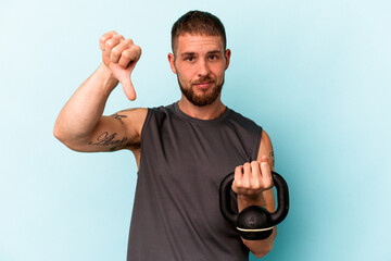 Young caucasian man holding ketlebell isolated on blue background showing a dislike gesture, thumbs...