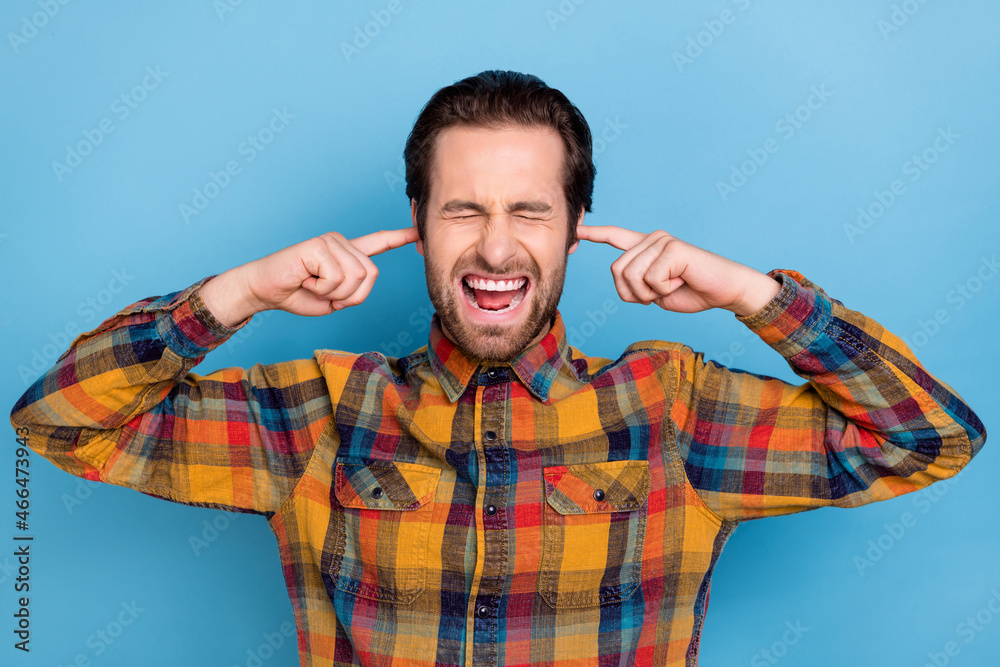 Poster photo of annoyed upset young man wear plaid shirt closed eyes fingers close ears isolated blue color