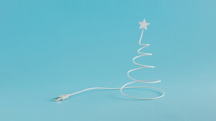 Creative digital Christmas arrangement made of USB cable in the shape of a Christmas tree on a blue background. Minimal New Year concept with copy space. Online holiday inspiration.