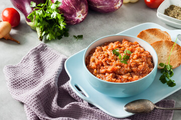 Eggplant caviar in blue bowl and fresh vegetables on background