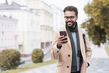 Young handsome student man using smartphone, Smiling joyful guy autumn portrait, Cheerful businessman wearing warm clothes texting on his mobile phone in a city