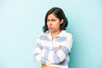Young latin woman isolated on blue background frowning face in displeasure, keeps arms folded.