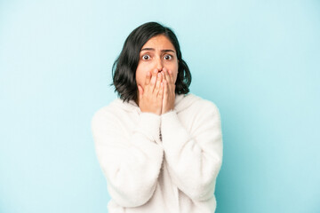 Young latin woman isolated on blue background covering mouth with hands looking worried.