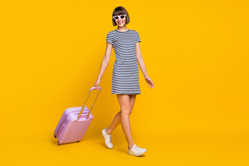 Full size photo of funky brunette millennial lady go with bag wear striped dress spectacles sneakers isolated on yellow background