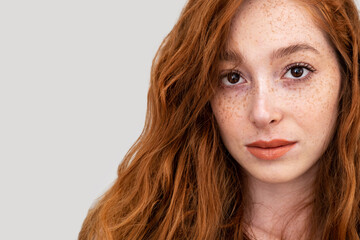 Face with freckles of a beautiful woman with red hair and lips isolated on gray background