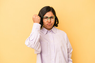 Young latin woman isolated on yellow background showing fist to camera, aggressive facial expression.