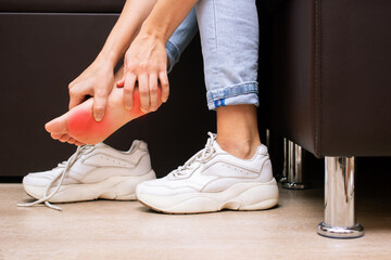 Pain in the feet from uncomfortable shoes. A woman holds a sore foot with hands sitting on a couch. Ache caused by wearing sneakers. Discomfort from walking for a long time. Orthodontics