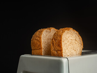 Rich and soft whole wheat bread in the toaster with a black background. Close-up photo. Space for text
