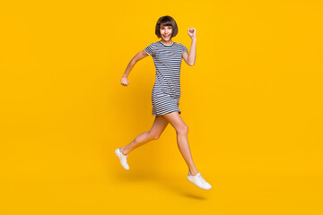 Fototapeta na wymiar Full body photo of funny young lady run wear striped dress sneakers isolated on yellow background