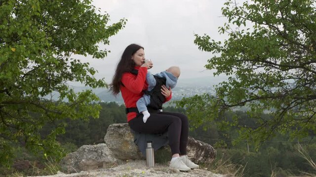 Woman with a baby in a sling ergo backpack traveling outdoor, family vacations adventure, mom with baby boy in infant kid carrier hiking. High quality 4k footage