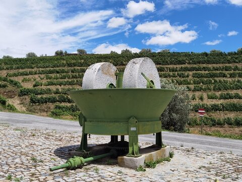 Monumento em estrada com uma m&aacute;quina de moer a azeitona para a produ&ccedil;&atilde;o do azeite com uma vinha ao fundo