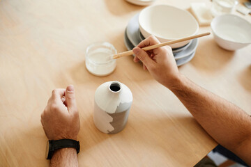 Close up of unrecognizable male artist decorating ceramics in pottery workshop, copy space