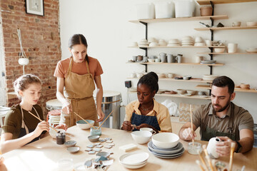 Warm toned shot of diverse group of people decorating ceramics in pottery workshop - Powered by Adobe