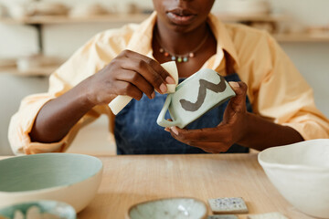 Close up of unrecognizable African-American woman decorating ceramics in pottery workshop, copy space - obrazy, fototapety, plakaty