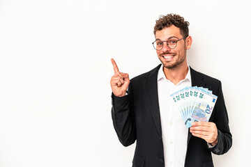 Young business caucasian man holding banknotes isolated on white background smiling and pointing aside, showing something at blank space.