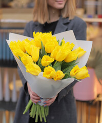 Beautiful yellow tulips bouquet. Young woman holding big bouquet of fresh tulips wrapped in paper.